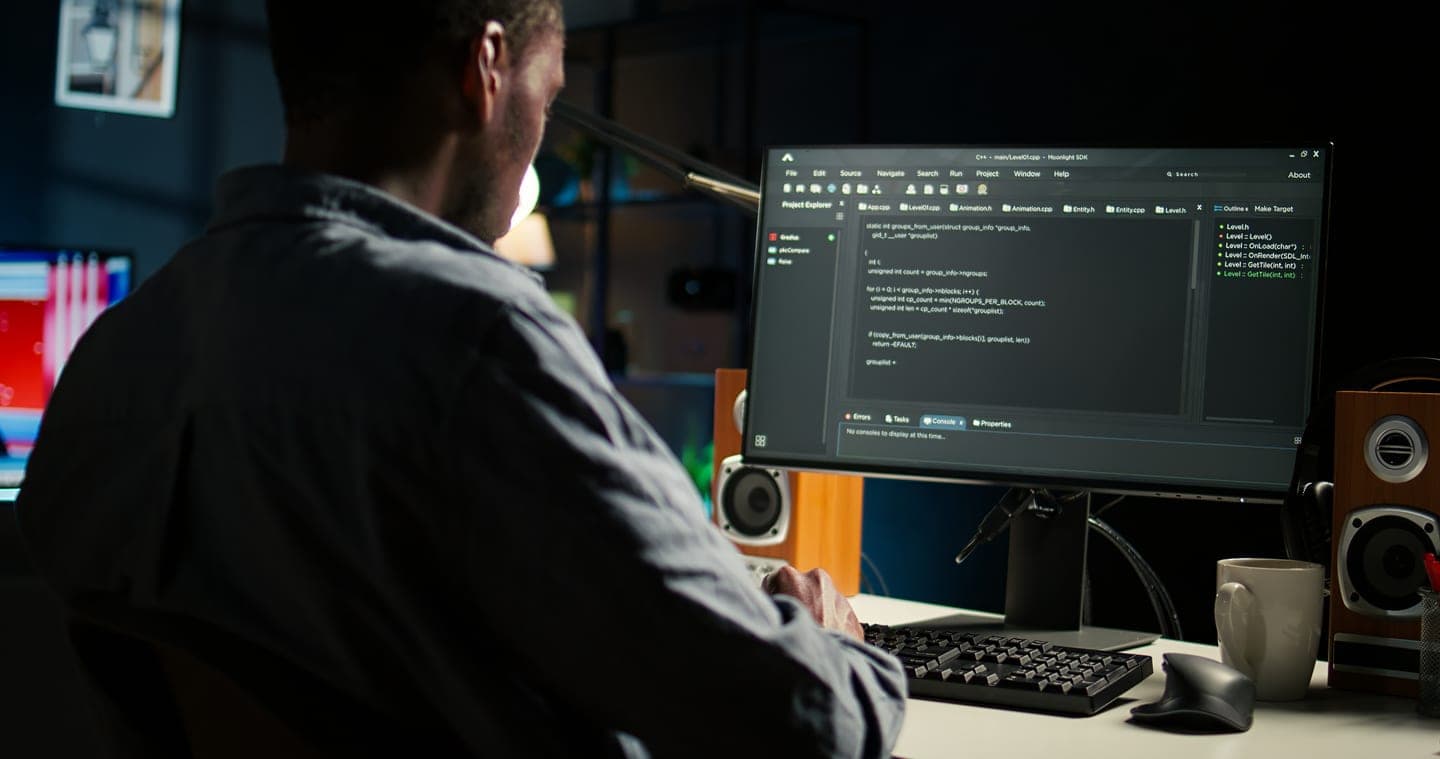 Developer seen from behind in a dimly lit room, working through code in an editor on a large monitor between two speakers