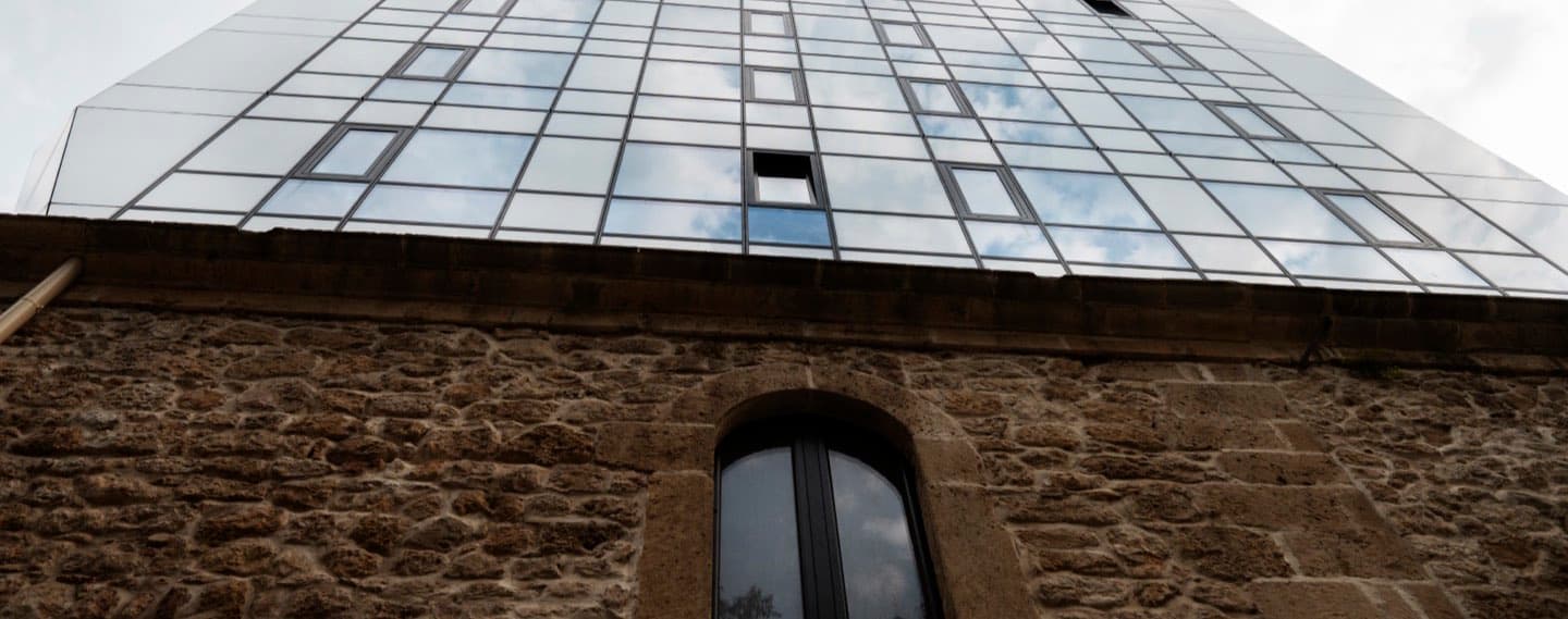 A modern glass storey built directly on top of an old stone building, seen from below.